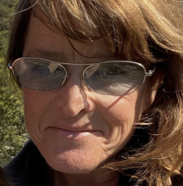 Juris Doctor, Connie Kratovil-Lavelle, with brown surfer hair, wearing sunglasses, and a smile while posing for a selfie outdoors.